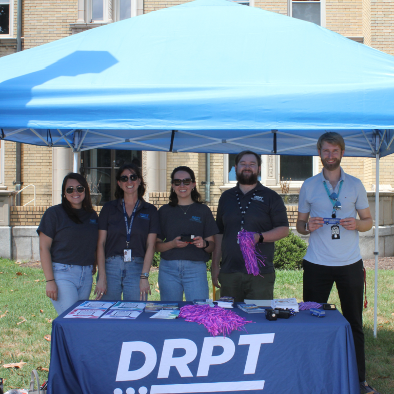 DRPT 員工在藍色帳篷下的 DRPT 品牌桌旁展示促銷品