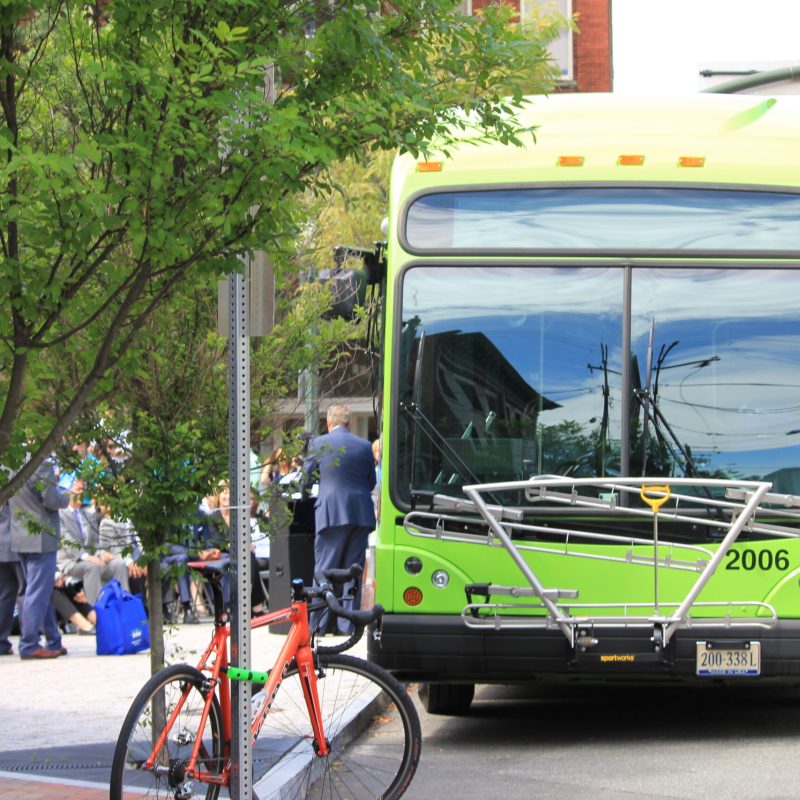 一輛巴士停在擁擠的人行道旁邊的照片圖像，背景為行人，前景是一輛自行車。